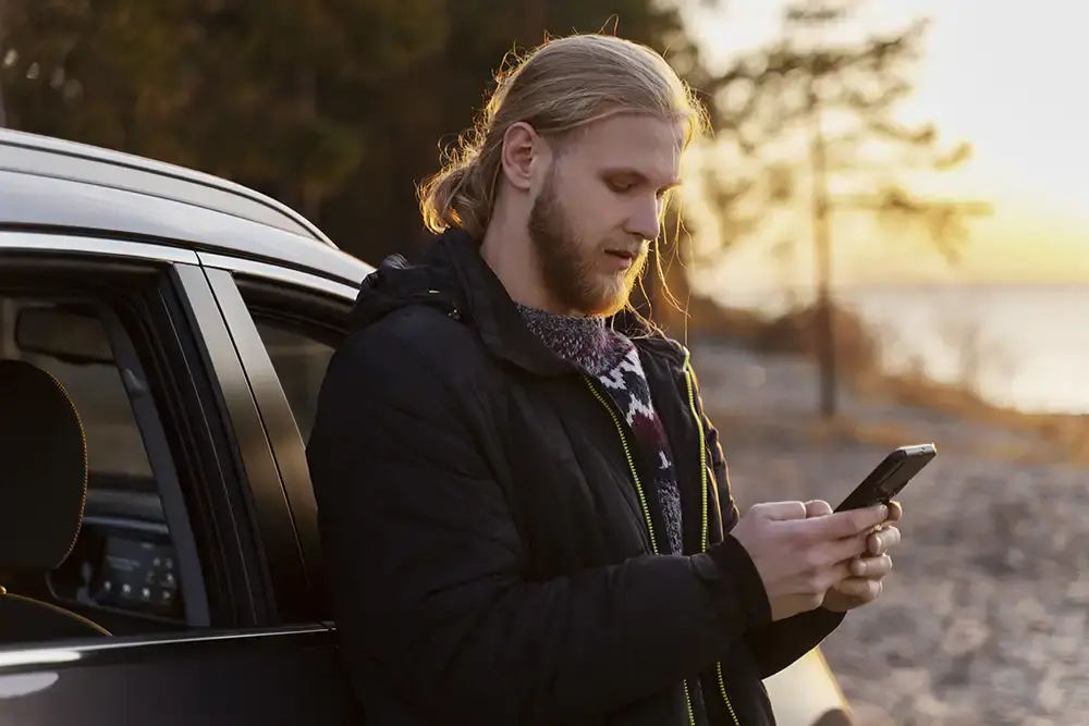 man som står och håller telefon vid en parkerad bil